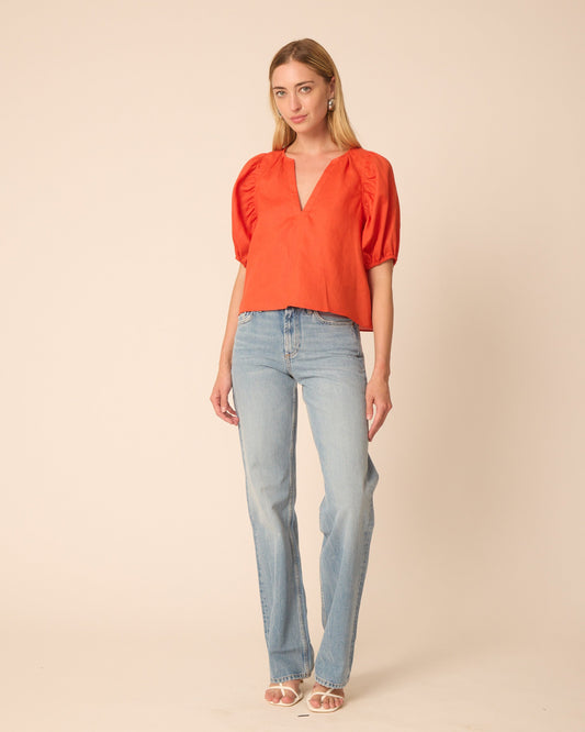 Woman wearing an orange blouse and light blue jeans on a beige background
