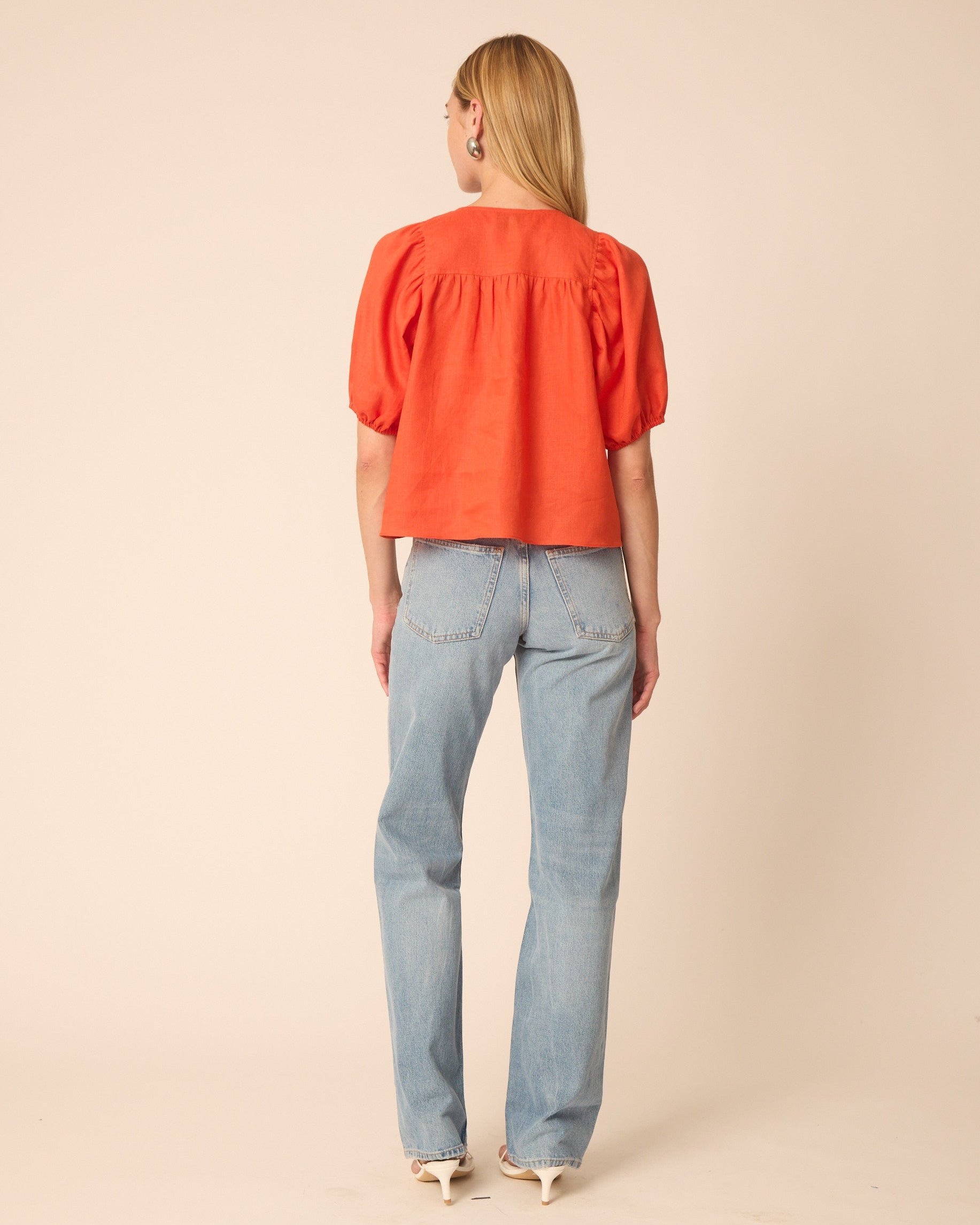 Woman wearing an orange blouse and light blue jeans on a beige background