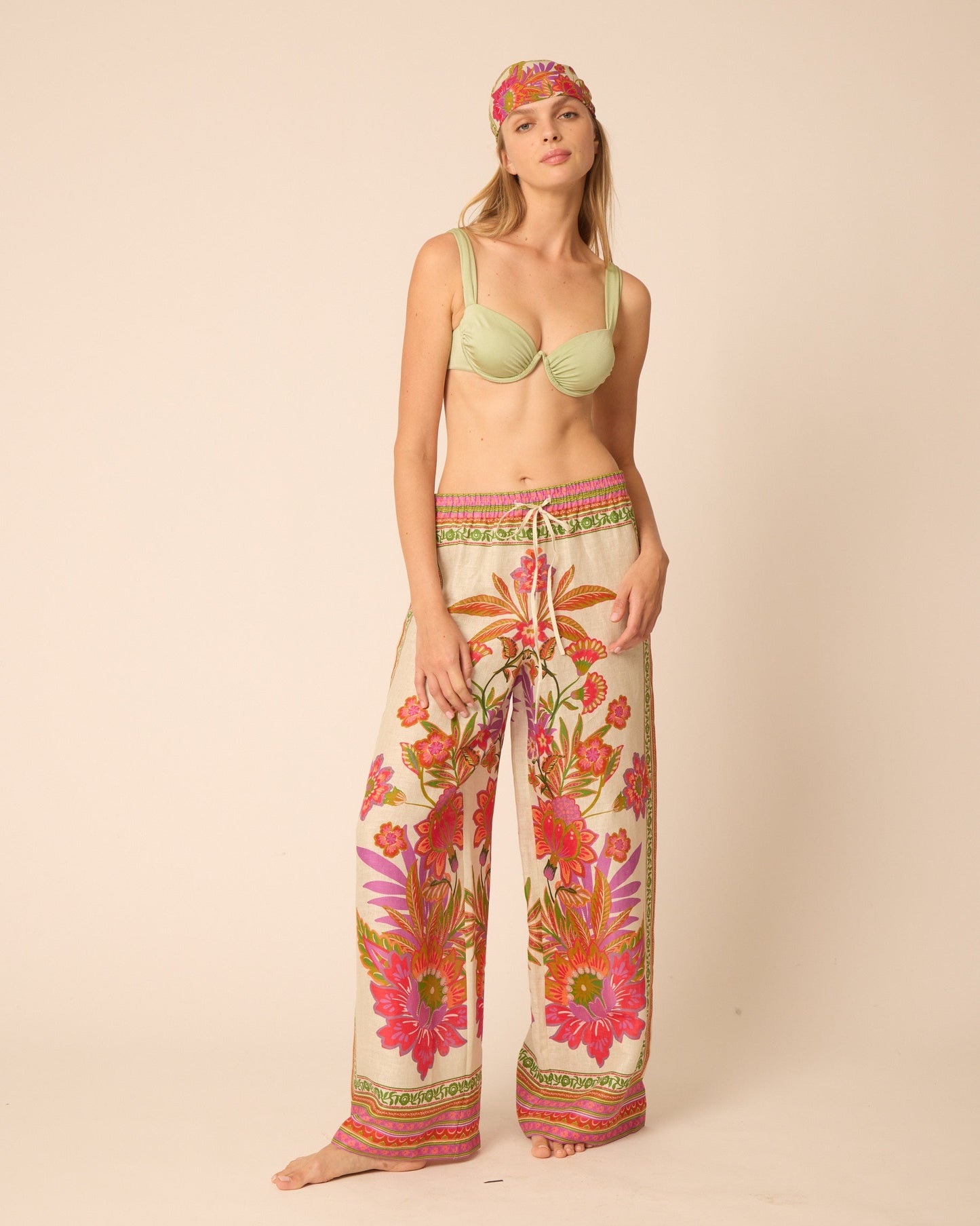 Woman wearing a light green bra and floral pants on a beige background
