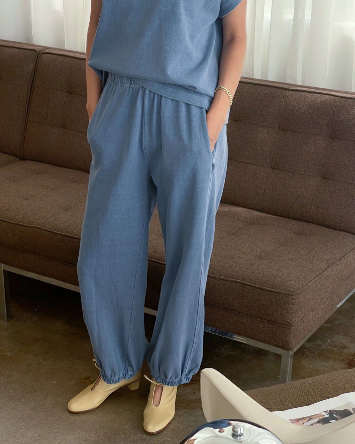 Person wearing a blue outfit standing in a room with a brown sofa.