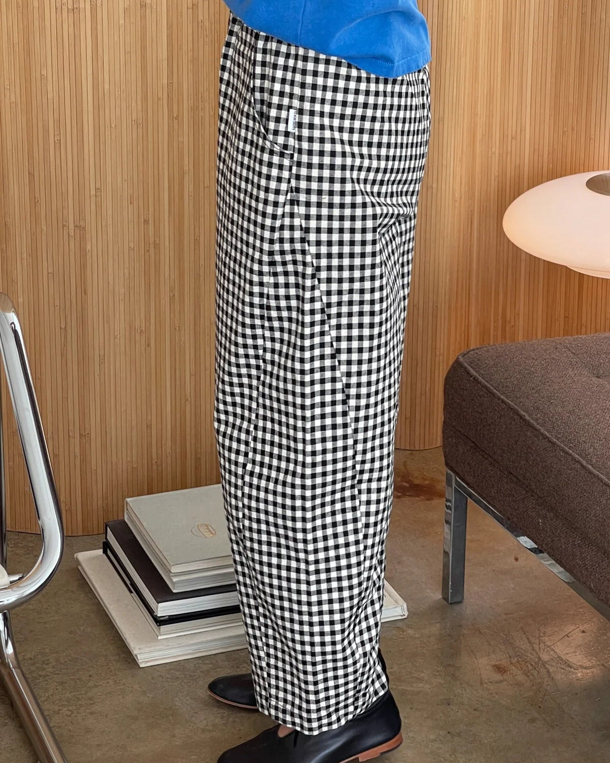 Person wearing black and white checkered pants in a room with wooden walls and furniture.