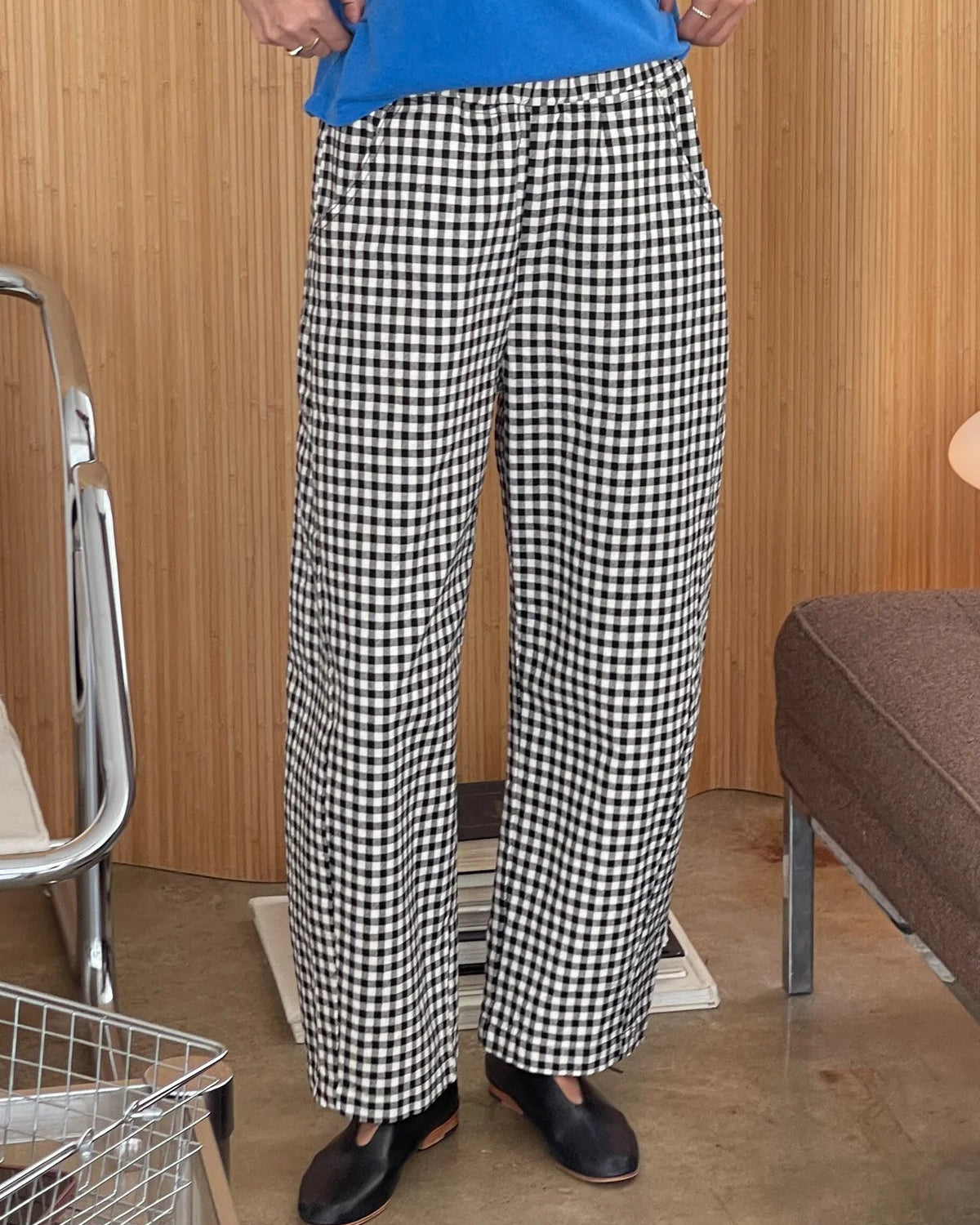Person wearing black and white checkered pants with a blue shirt in a room with wooden walls and furniture.