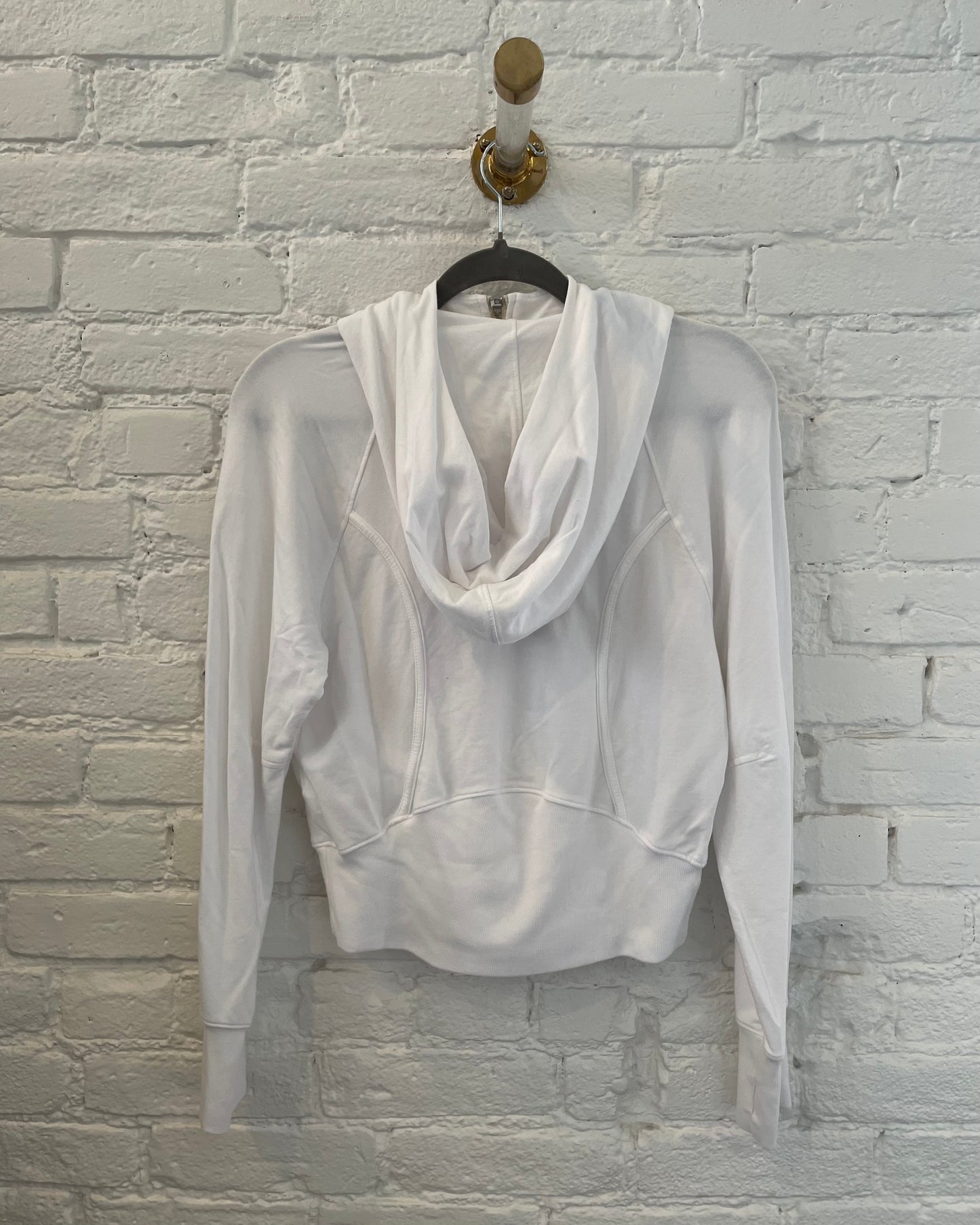 White hoodie on a hanger against a white brick wall