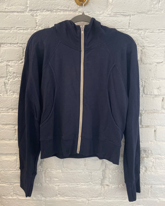 Navy blue hoodie with a zipper on a hanger against a light brick wall.