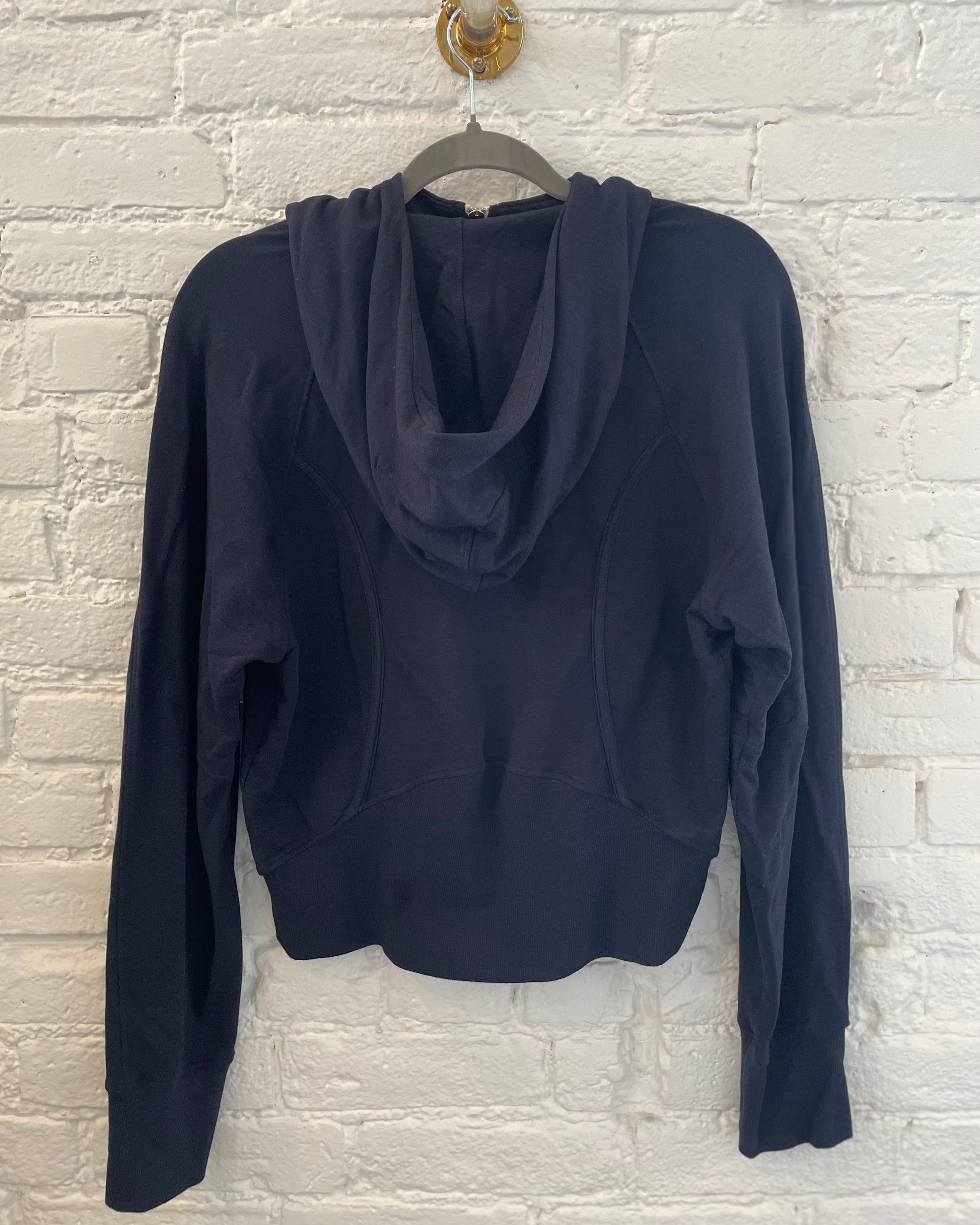 Navy blue hoodie on a hanger against a white brick wall.