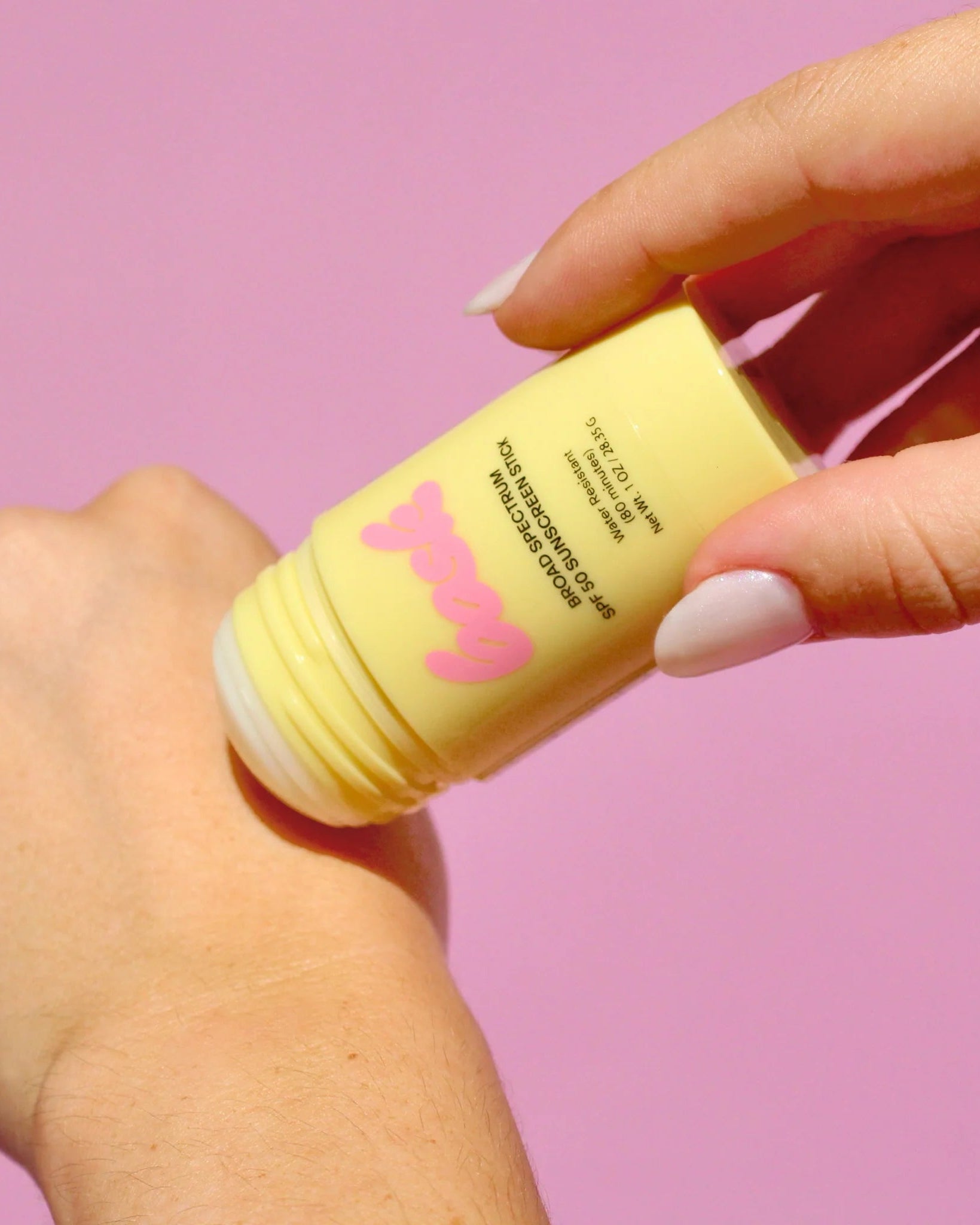Hand holding a yellow skincare product with a pink logo against a pink background