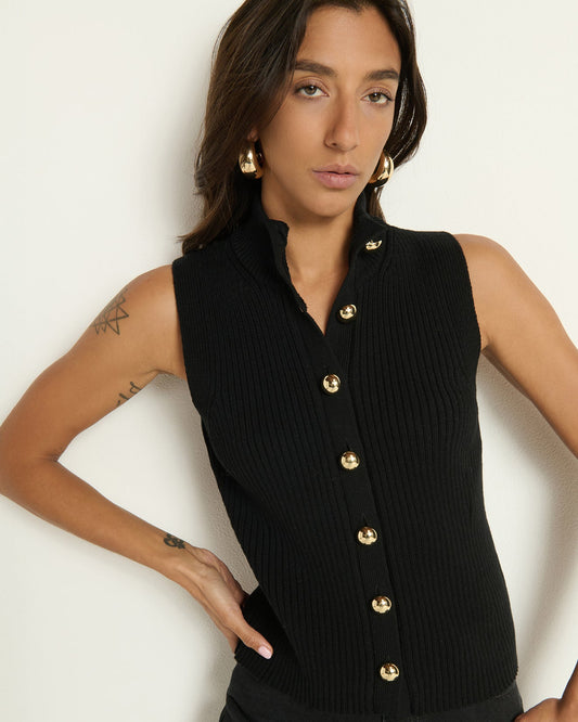 Model wearing a sweater vest with gold buttons standing in front of a white background