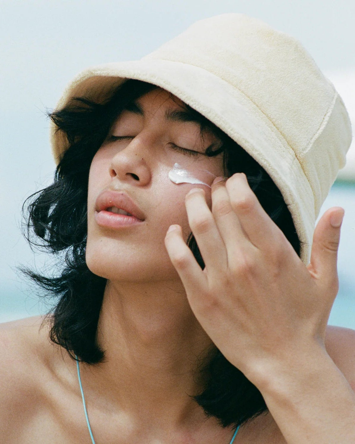 Woman applying sunscreen on her face with a beige bucket hat