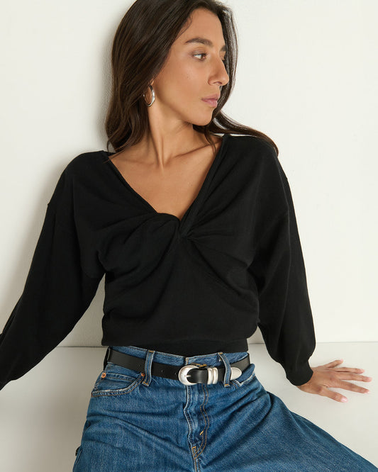 Model wearing Nation Jolie sweater in Jet Black with jeans sitting against a white wall background