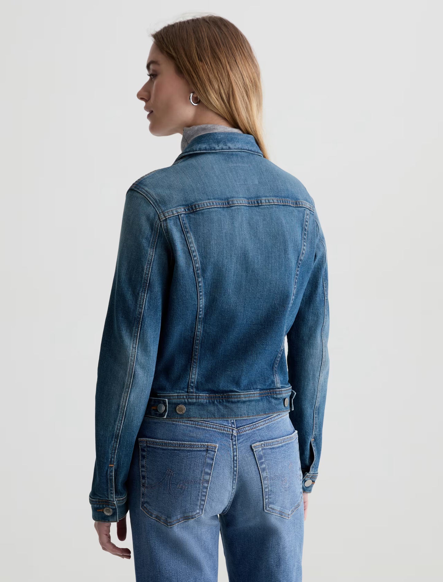 Woman wearing a blue denim jacket and jeans on a light gray background
