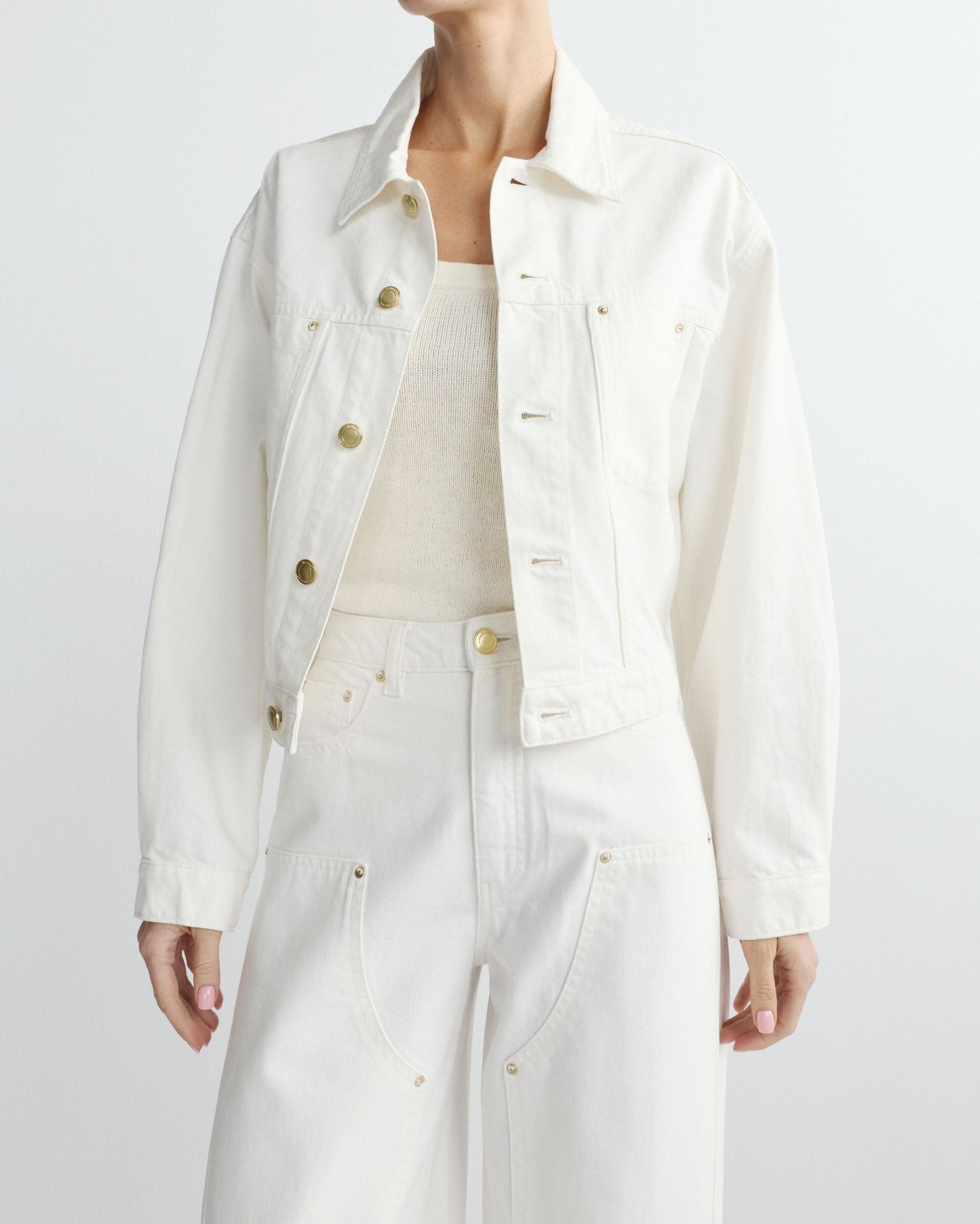 Person wearing a white denim jacket and pants on a light gray background