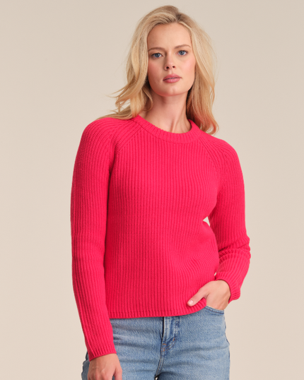 Woman wearing a bright pink sweater and blue jeans on a beige background