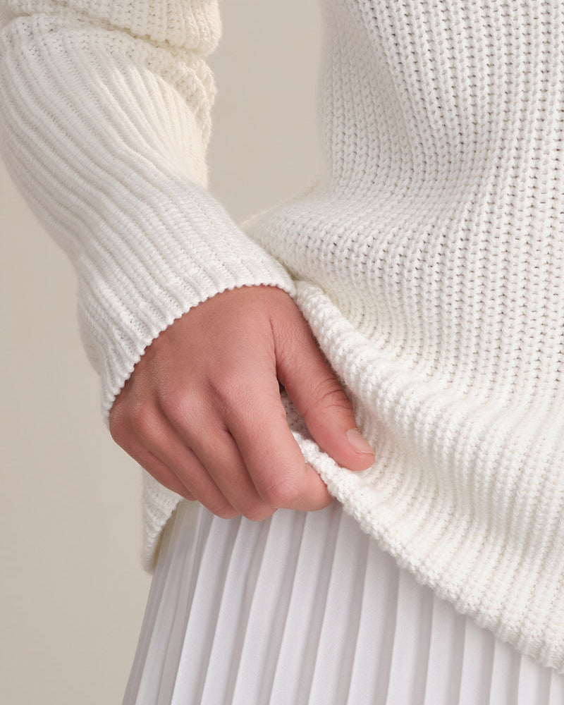 Close-up of a person wearing a white ribbed sweater with a neutral background