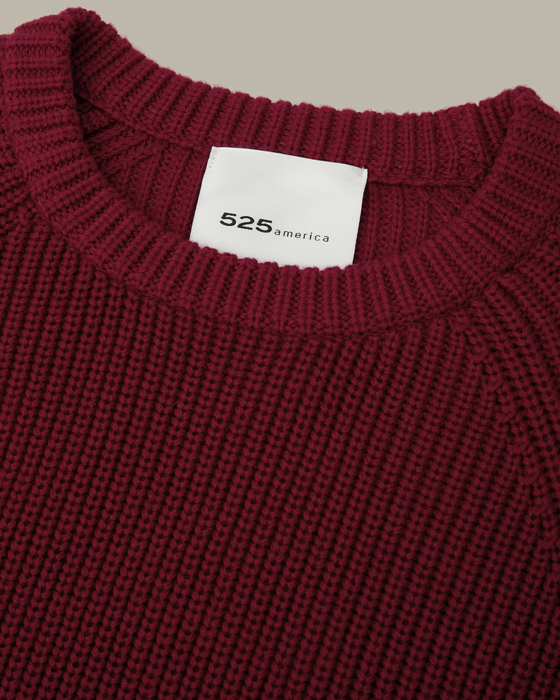 Close-up of a ribbed knit crewneck sweater in deep burgundy, showing a white neck label with the brand name '525america' printed in black.