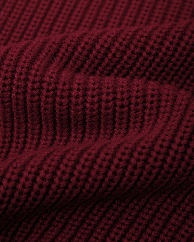 A close-up of a dark burgundy ribbed knit fabric, showing the detailed texture of the yarn and stitching.