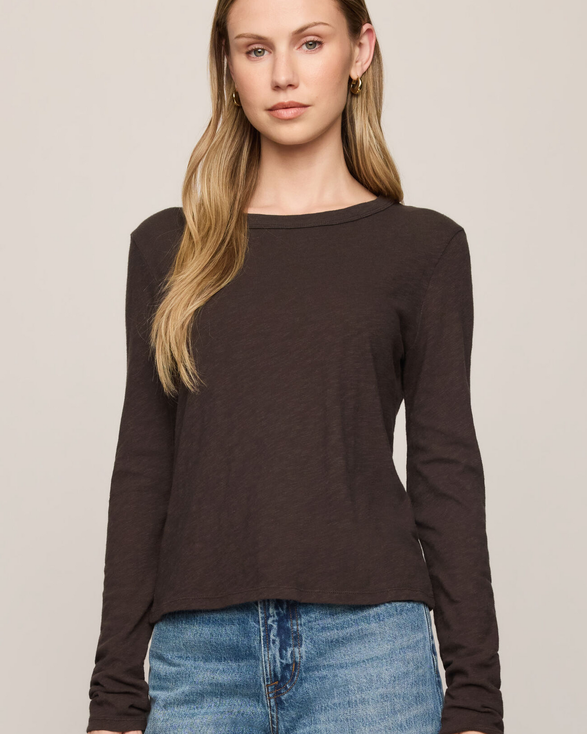 Woman wearing a black long-sleeve top and blue jeans against a plain background