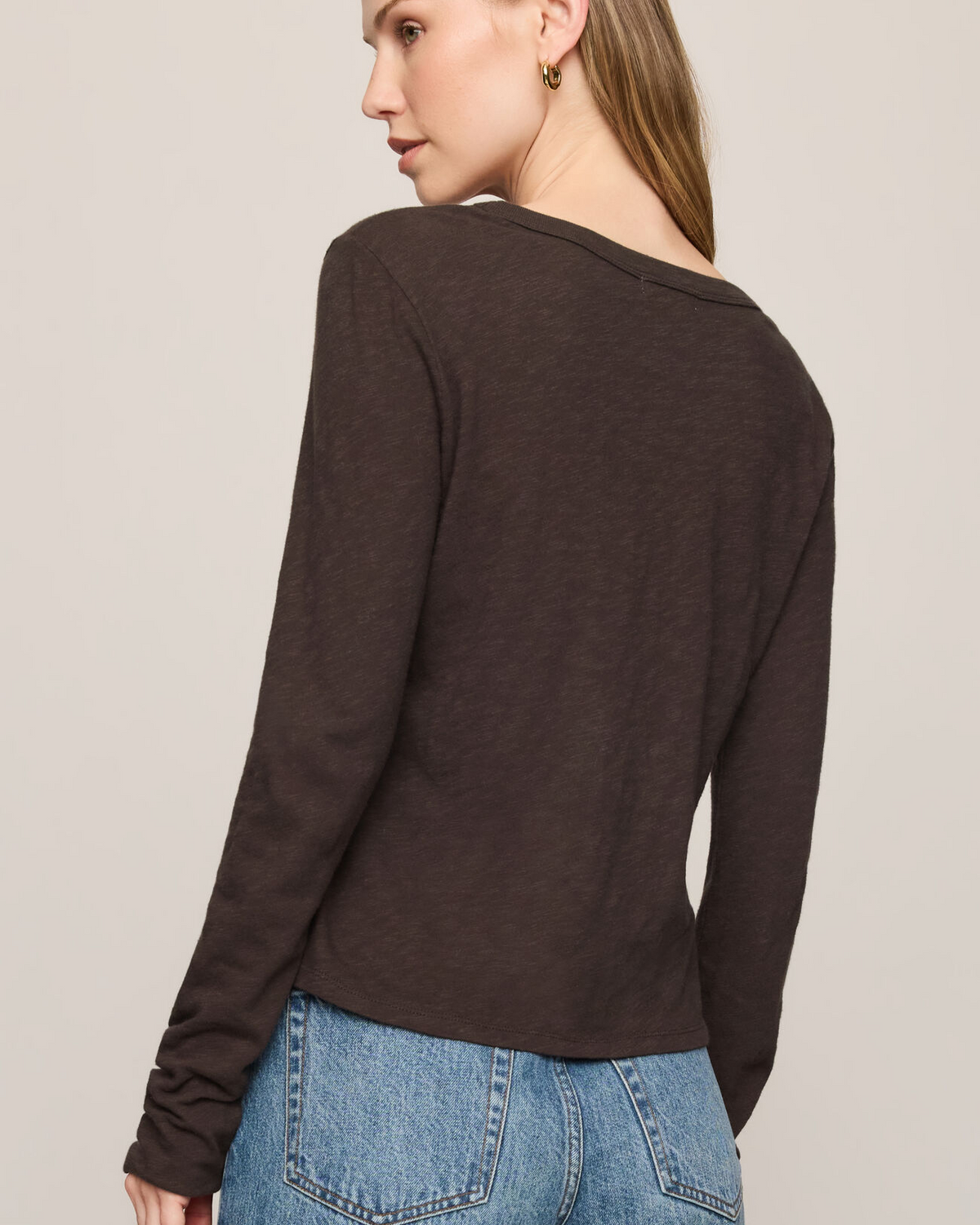 Woman wearing a dark brown long-sleeve top and blue jeans on a plain background