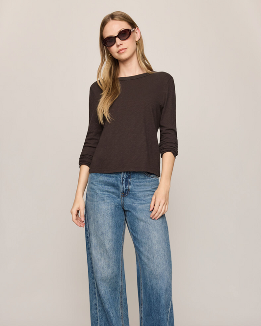 A woman modeling a dark brown long-sleeve knit top and wide-leg blue jeans against a plain light gray studio background.