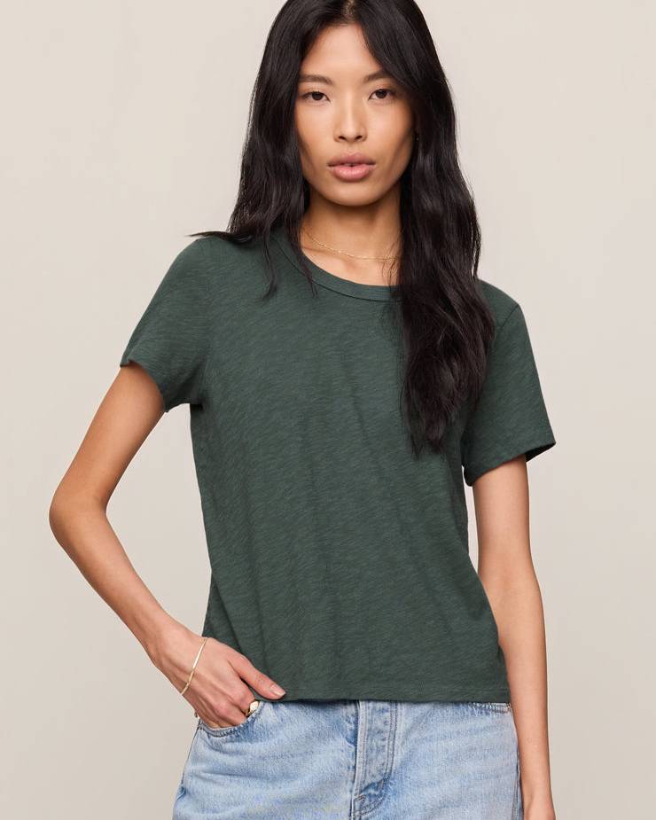 Woman wearing a green t-shirt and blue jeans against a plain background