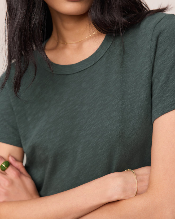 Person wearing a green t-shirt with arms crossed against a neutral background