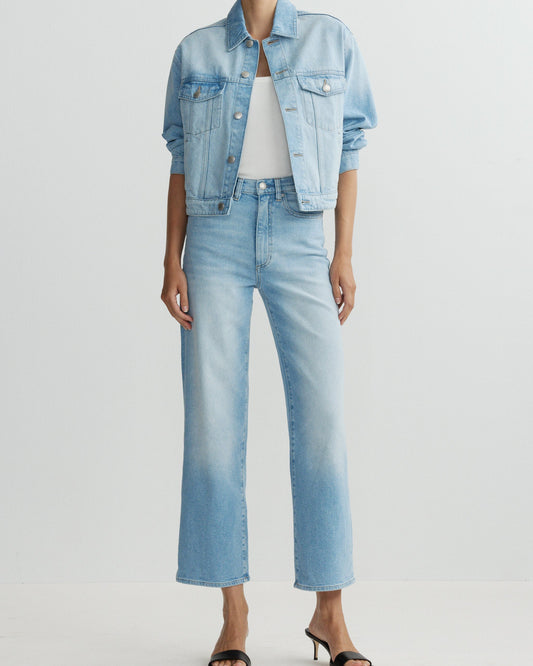 Person wearing a light blue denim jacket and jeans on a white background