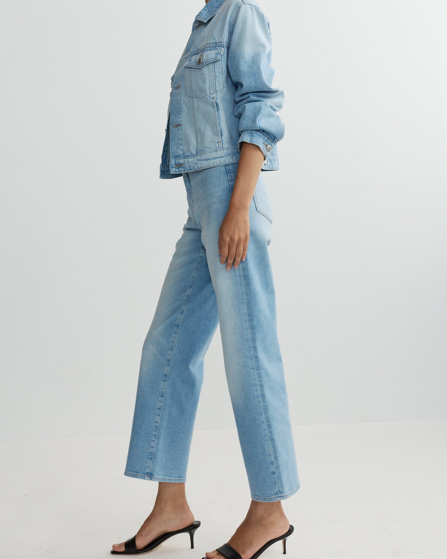 Person wearing a light blue denim jacket and jeans on a white background