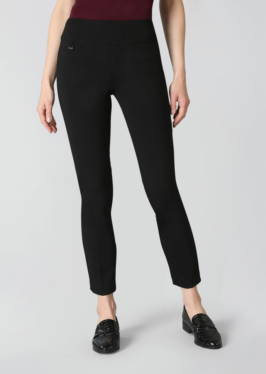 A model wearing black slim-fit ankle-length trousers with a small black rectangular logo patch on the left hip, paired with a burgundy top and black patent leather loafers, against a light gray studio background.