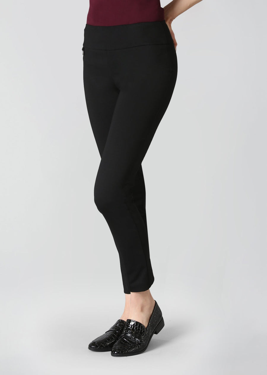 A person modeling black slim-fit ankle-length pants with a wide waistband, paired with black loafers, against a light gray studio background.