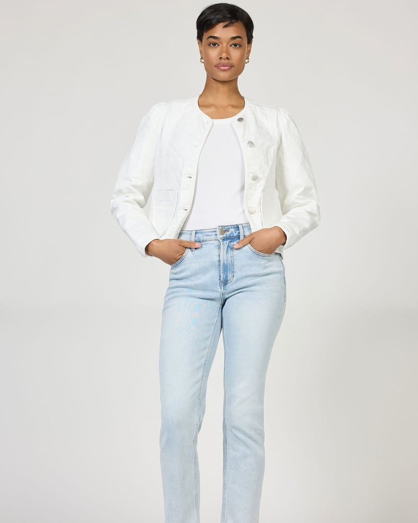 Woman wearing a white jacket and light blue jeans on a plain background