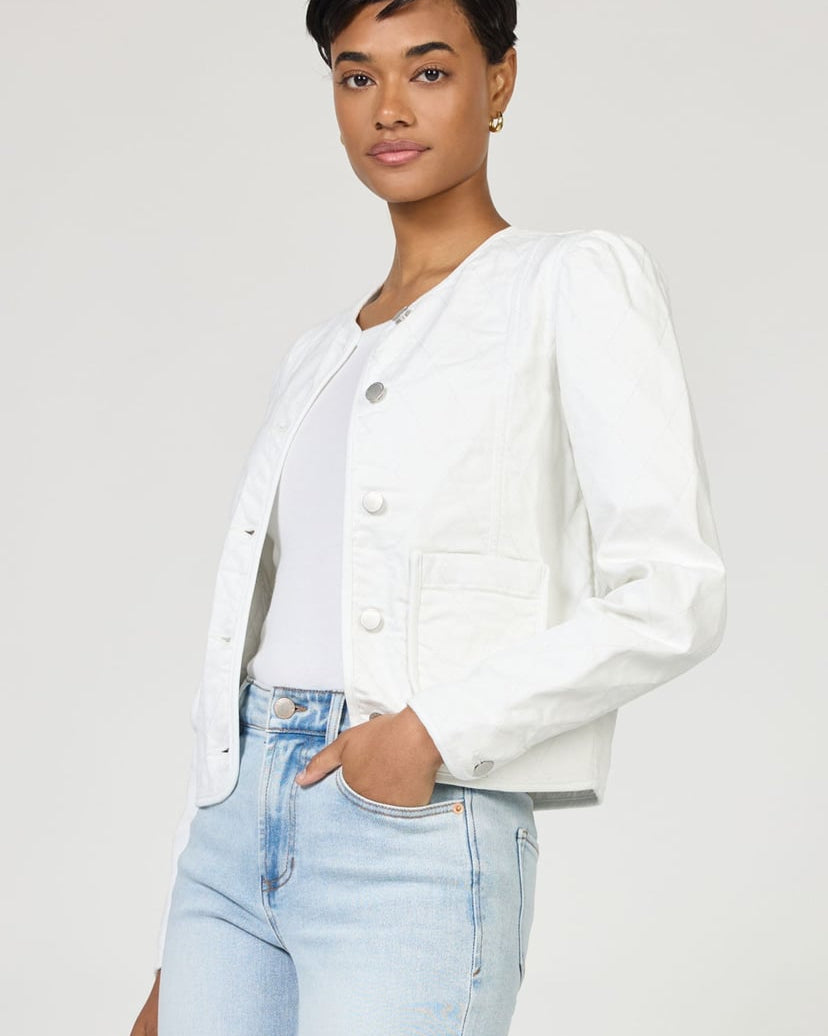 Woman wearing a white jacket and light blue jeans on a plain background