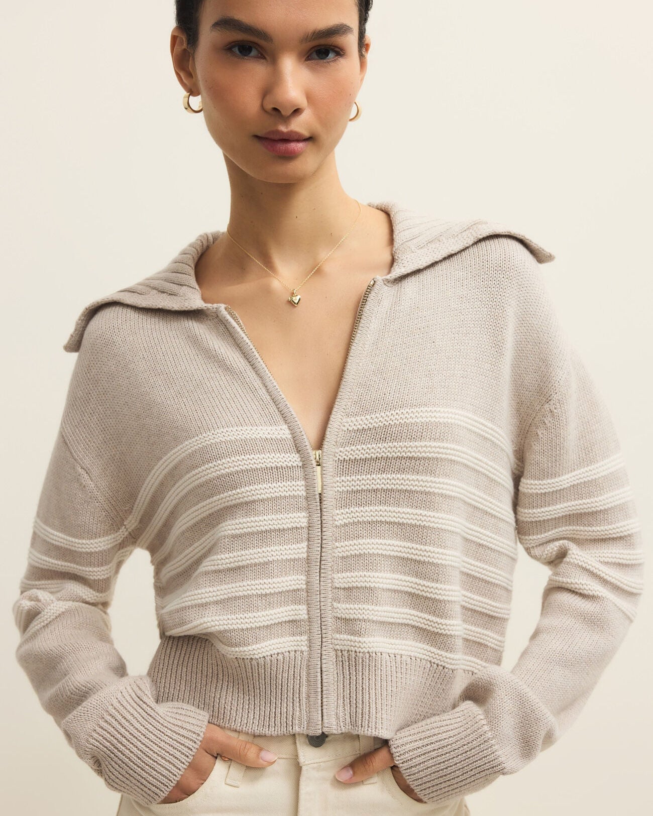 Woman wearing a beige zip-up sweater against a plain background