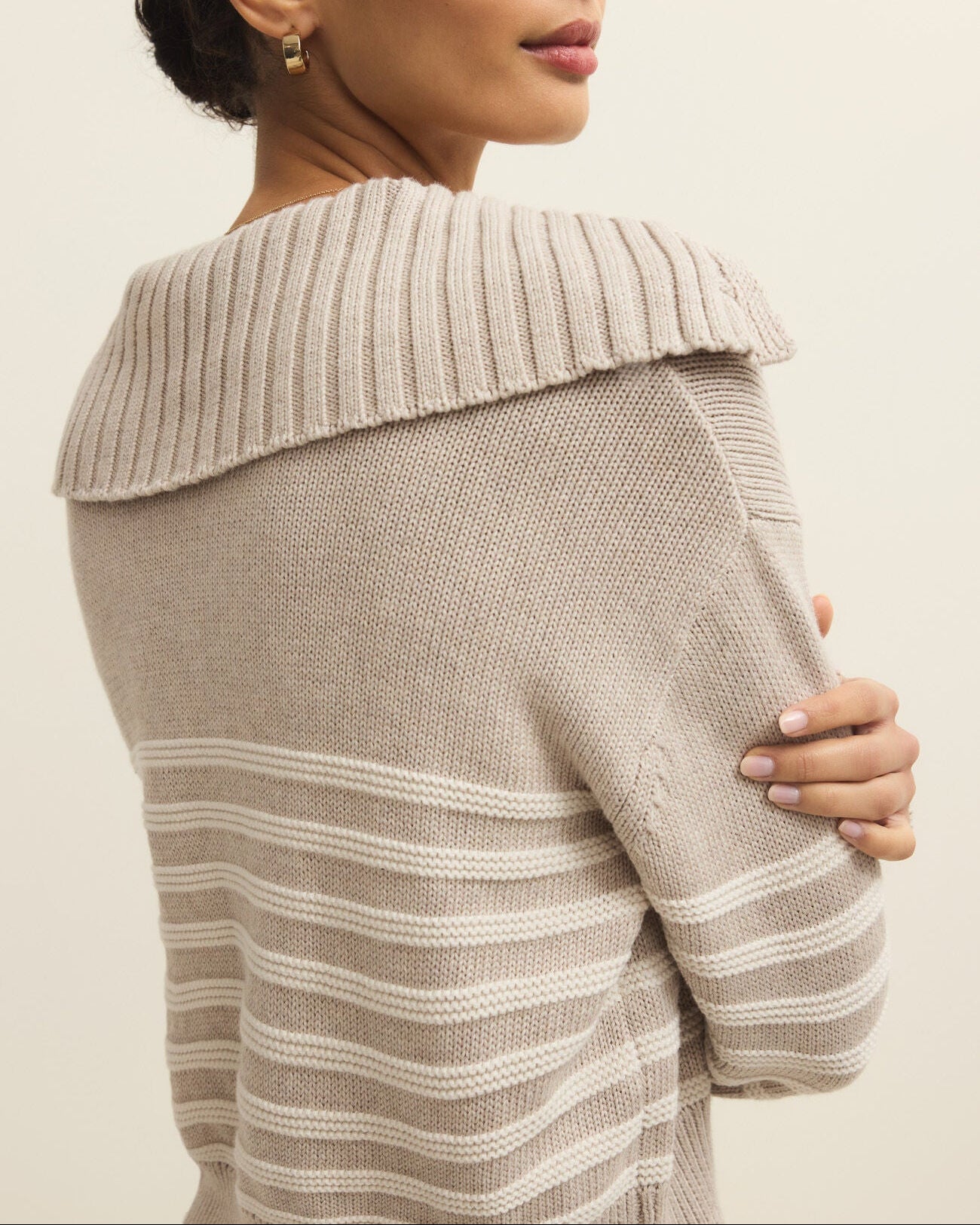 Woman wearing a beige sweater with a textured collar against a plain background