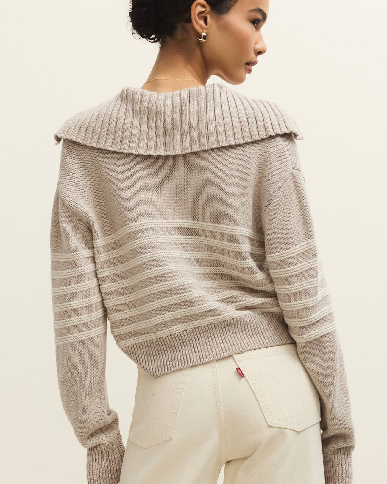 Woman wearing a beige sweater with a textured collar against a plain background