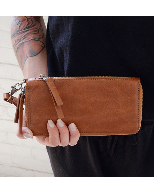 Person holding a chicory vegan leather wallet against a white brick wall.