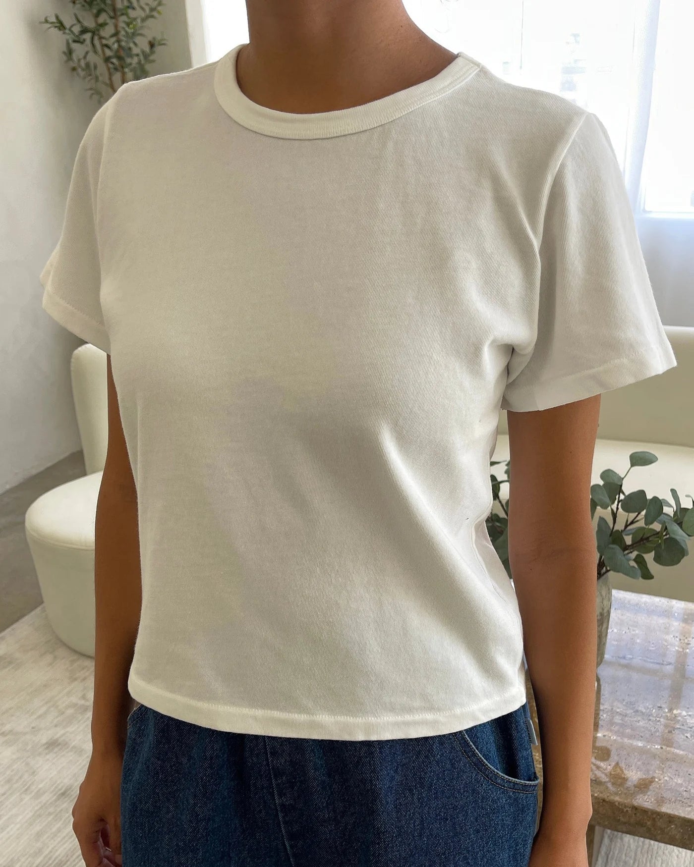 Person wearing a plain white t-shirt and blue jeans indoors.