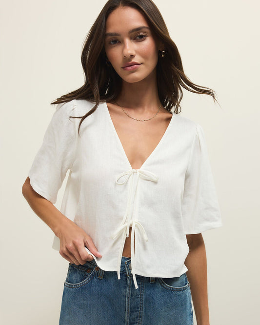 Woman wearing a white blouse with a tie front and blue jeans on a plain background