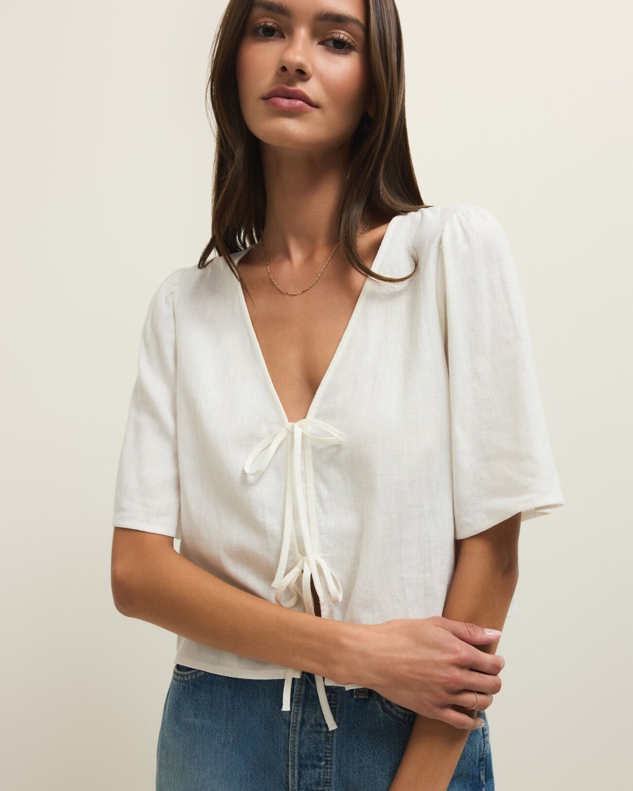 Woman wearing a white blouse with short sleeves and blue jeans on a plain background