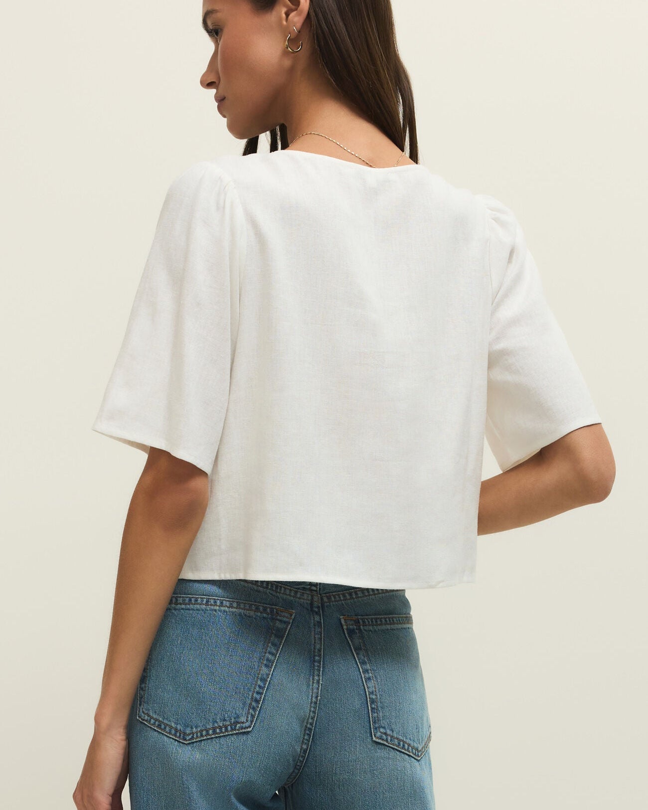 Woman wearing a white top and blue jeans against a plain background