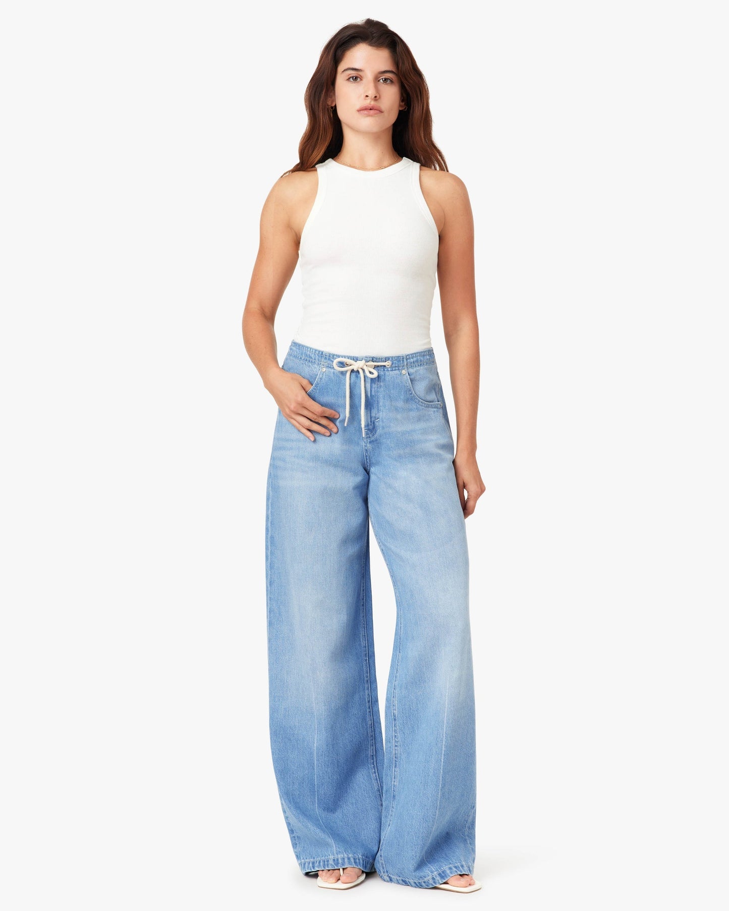Woman wearing a white sleeveless top and light blue jeans on a white background
