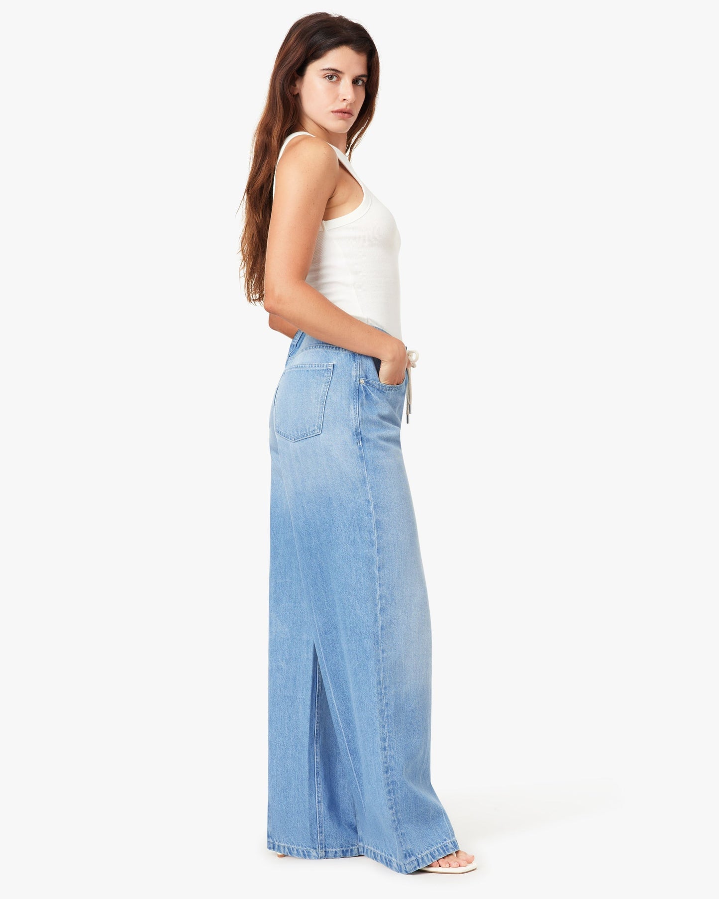 Woman wearing a white top and light blue denim pants on a white background