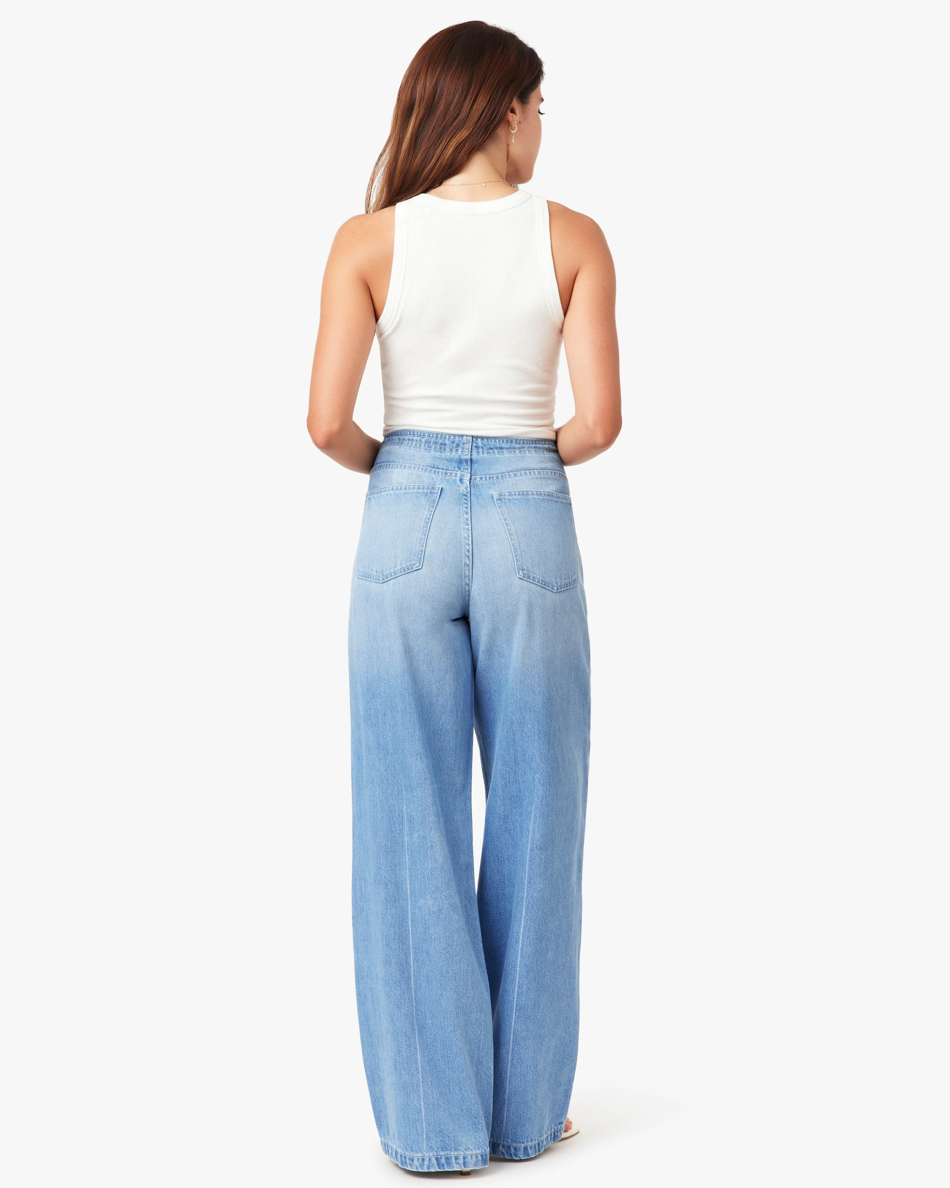 Woman wearing light blue jeans and a white top on a white background