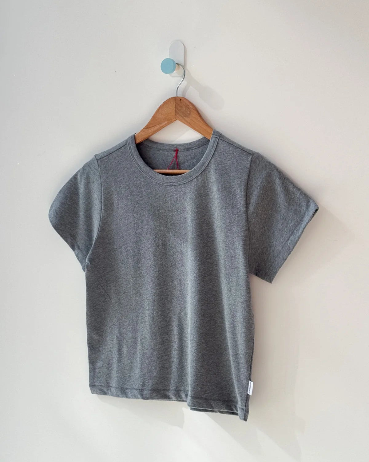 Gray t-shirt on a wooden hanger against a white wall
