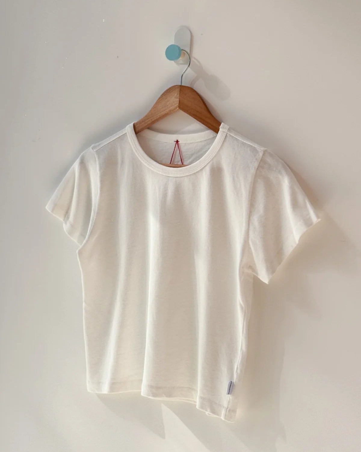 White t-shirt on a wooden hanger against a white wall