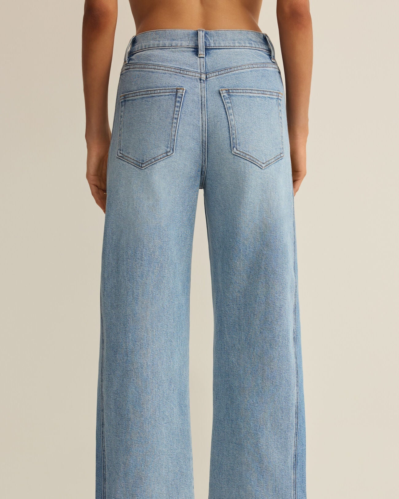 Light blue wide-leg jeans worn by a person on a beige background