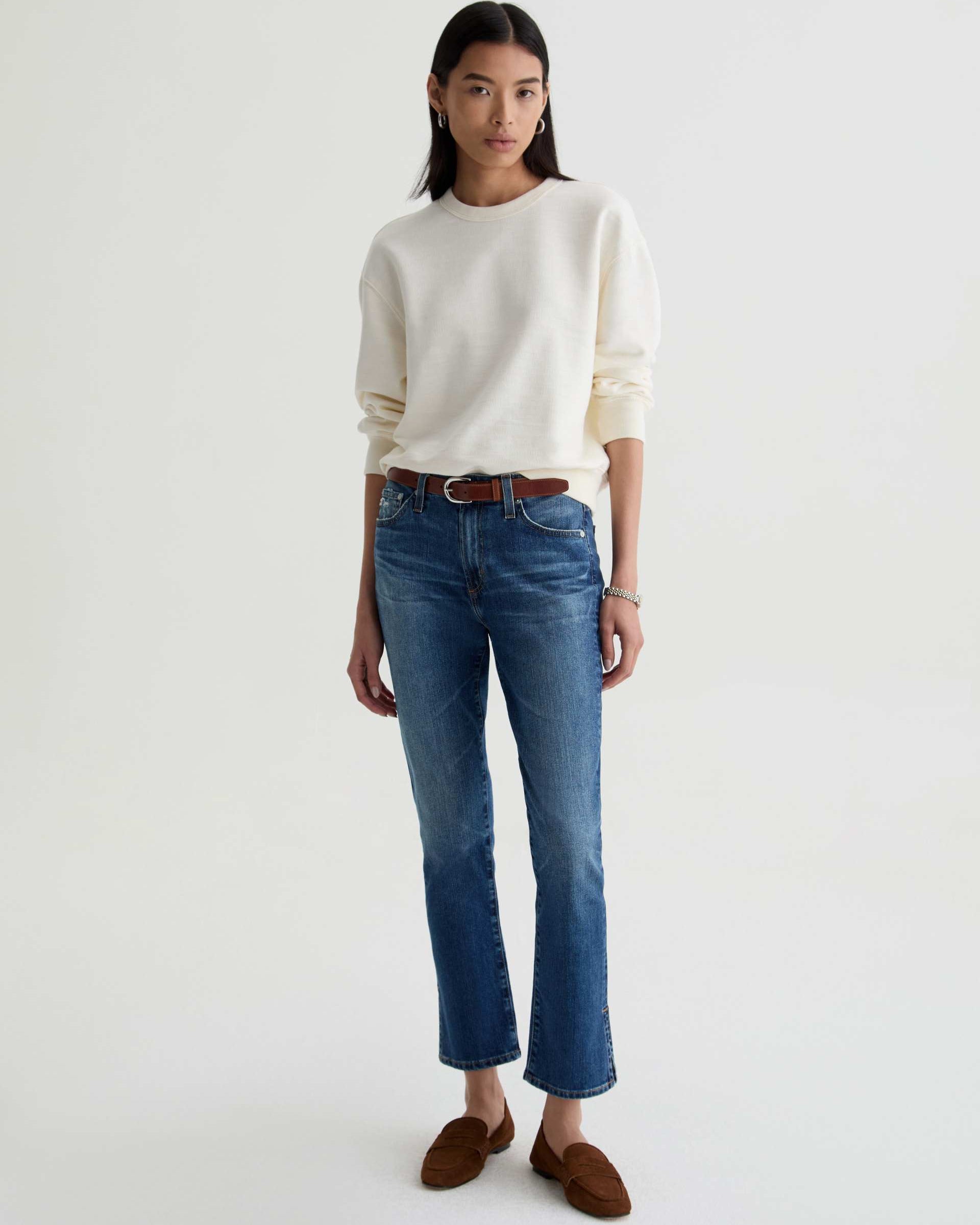 Woman wearing a white sweater and blue jeans on a white background