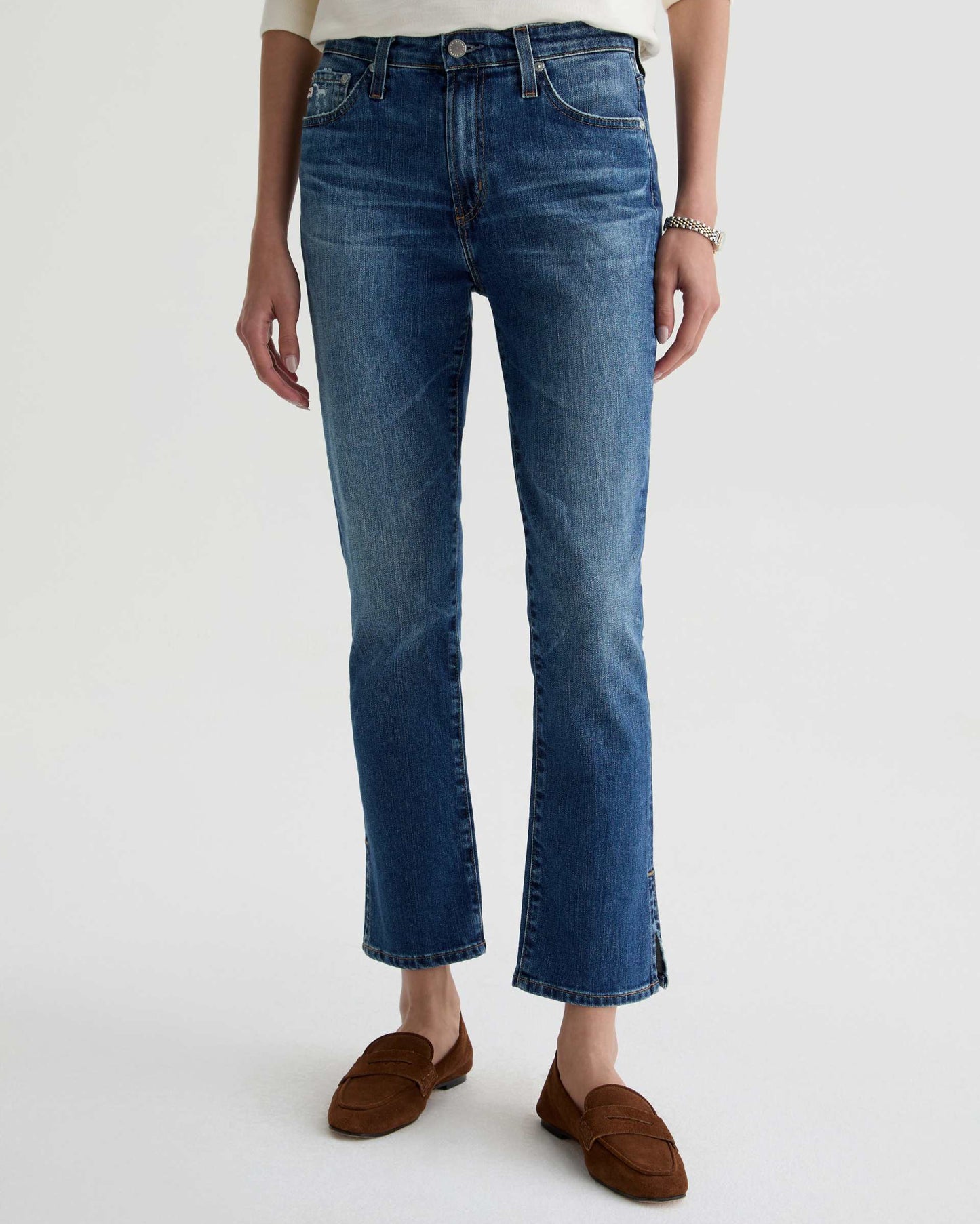 Person wearing blue jeans and brown shoes on a white background