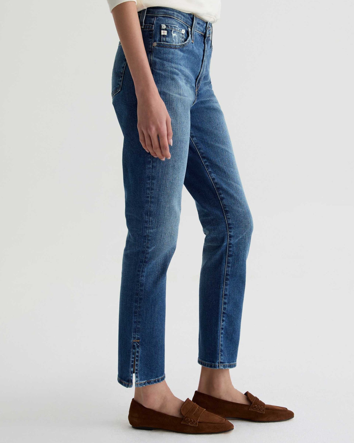 Person wearing blue jeans and brown shoes on a white background