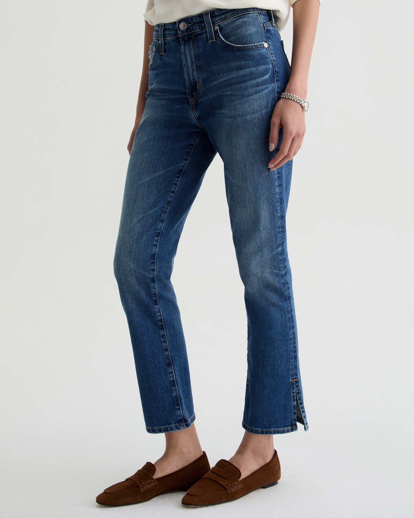 Person wearing blue jeans and brown loafers on a white background