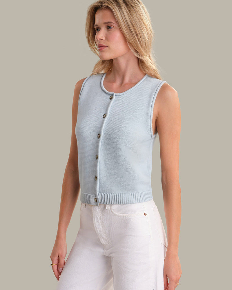 Woman wearing a light blue sleeveless cardigan against a neutral background