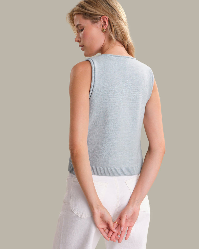 Woman wearing a light blue sleeveless sweater against a neutral background